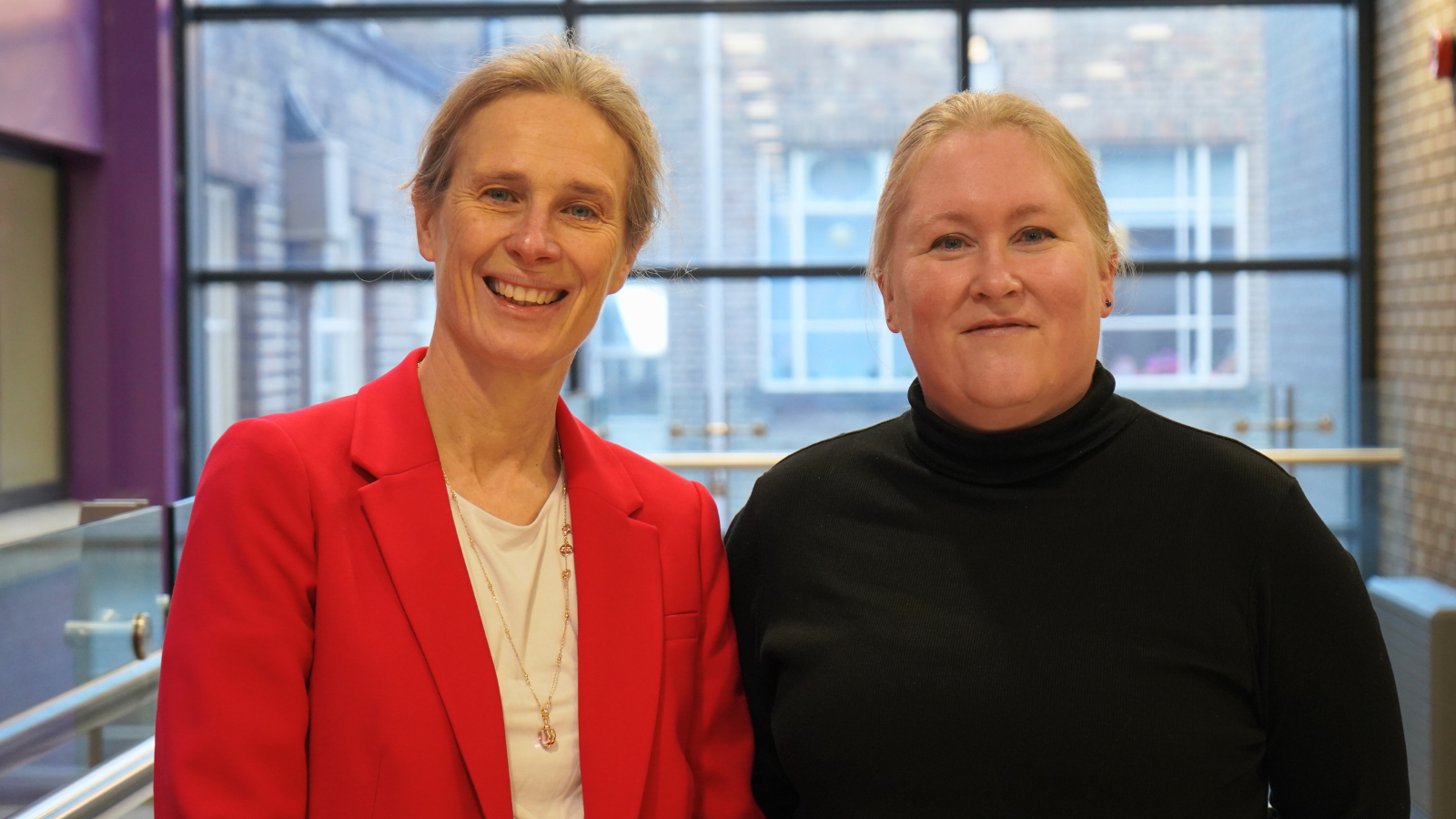 Head and shoulders shot of two women standing up with a window behind them
