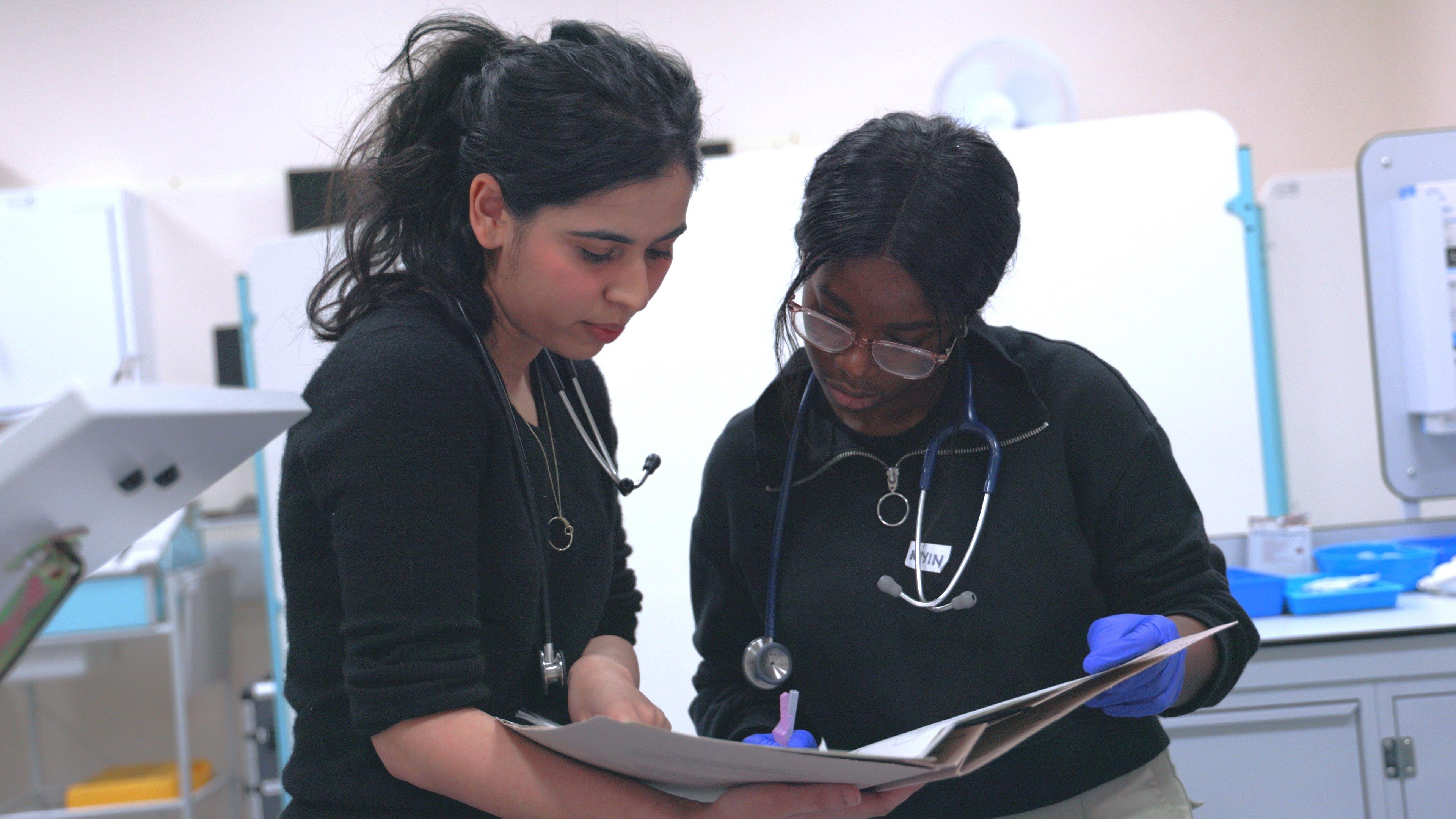 Two Doctors stood discussing whilst looking at some patient notes.